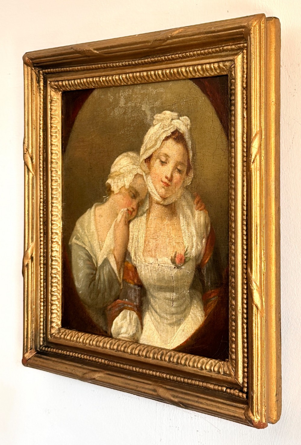 An 18th-century oil painting on canvas depicting two women in period costume within an oval painted border, housed in a carved gilded frame. View V