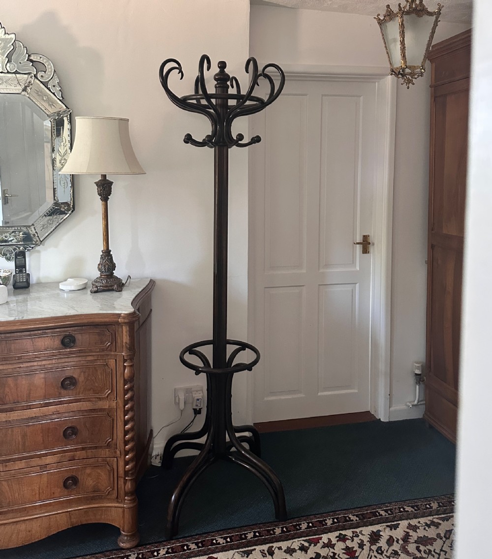 A tall dark brown bentwood coat and hat stand featuring double curved hooks, a central turned column, an umbrella drip ring, and splayed legs. View IV