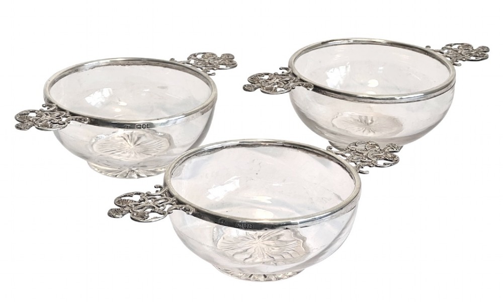 A set of three clear glass bowls featuring sterling silver rims and pierced scroll handles.