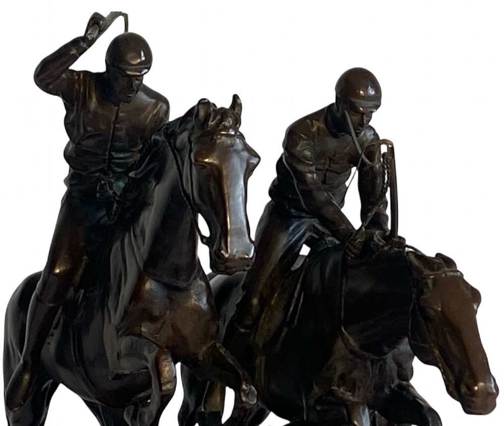 A dark brown bronze sculpture depicting two racehorses and jockeys clearing a fence during a steeplechase, mounted on a polished green marble base. View VI