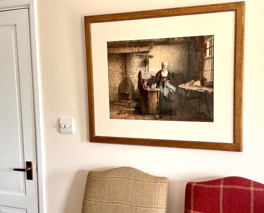 A framed 19th-century watercolour painting depicting a woman seated beside a child in a traditional Dutch kitchen interior with a tiled fireplace. View X