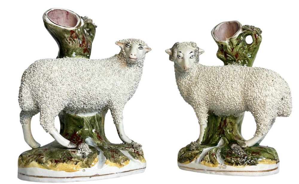 A pair of Victorian Staffordshire earthenware spill vases depicting textured woolly sheep standing alongside green tree trunk vessels.