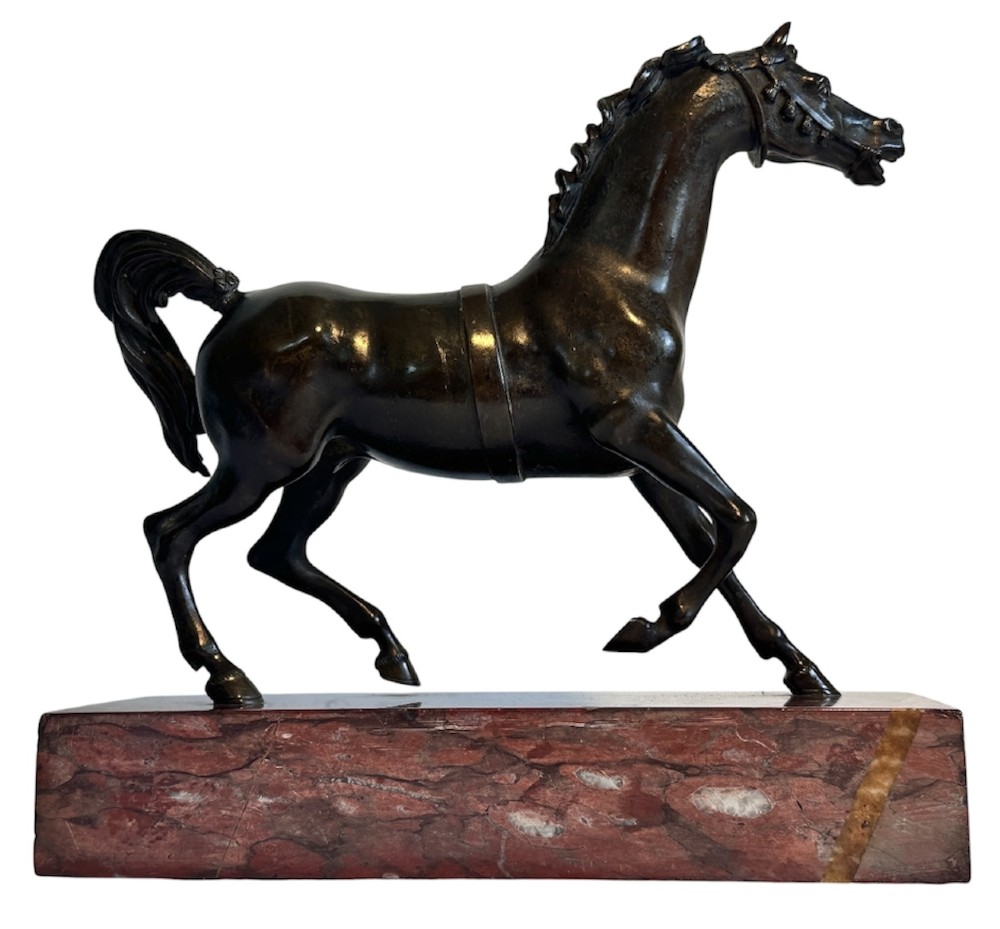 A dark patinated bronze sculpture of a trotting stallion mounted on a rectangular veined red marble plinth. View II