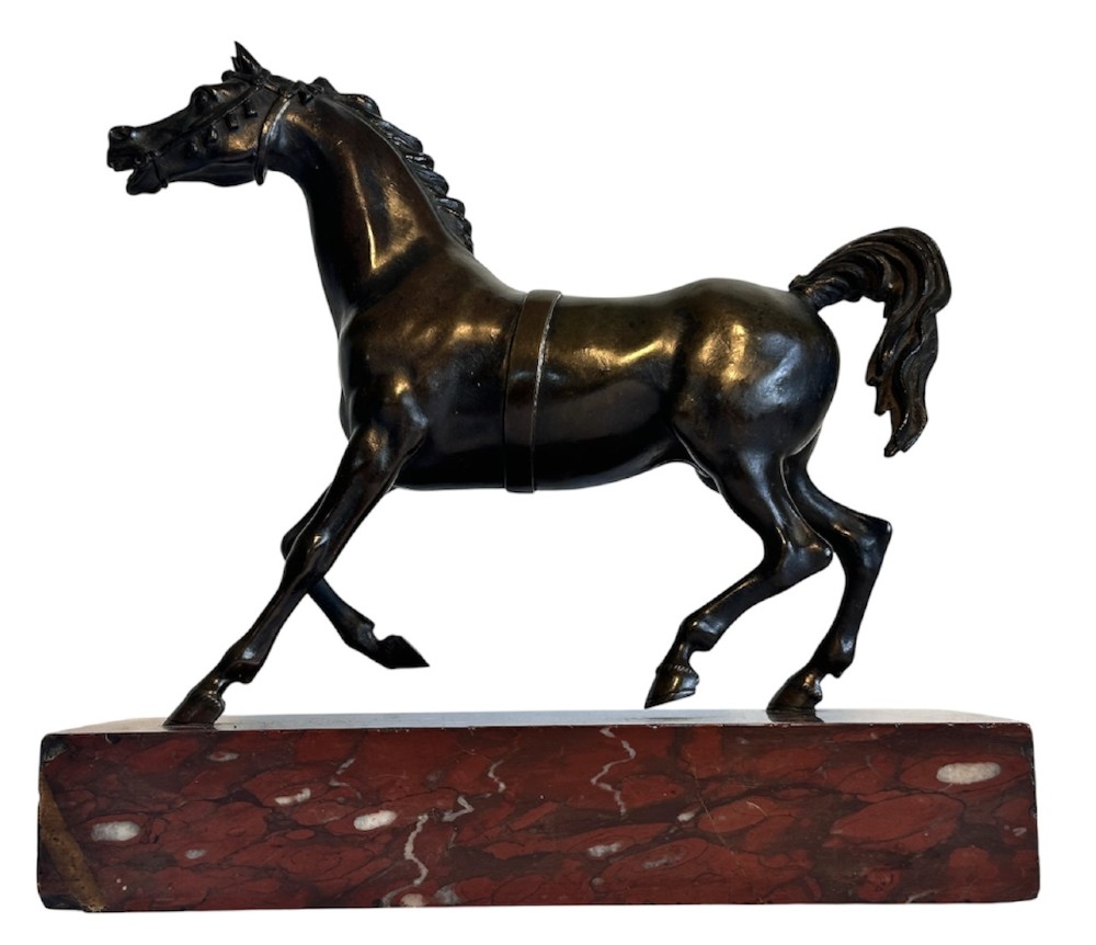 A dark patinated bronze sculpture of a trotting stallion mounted on a rectangular veined red marble plinth.
