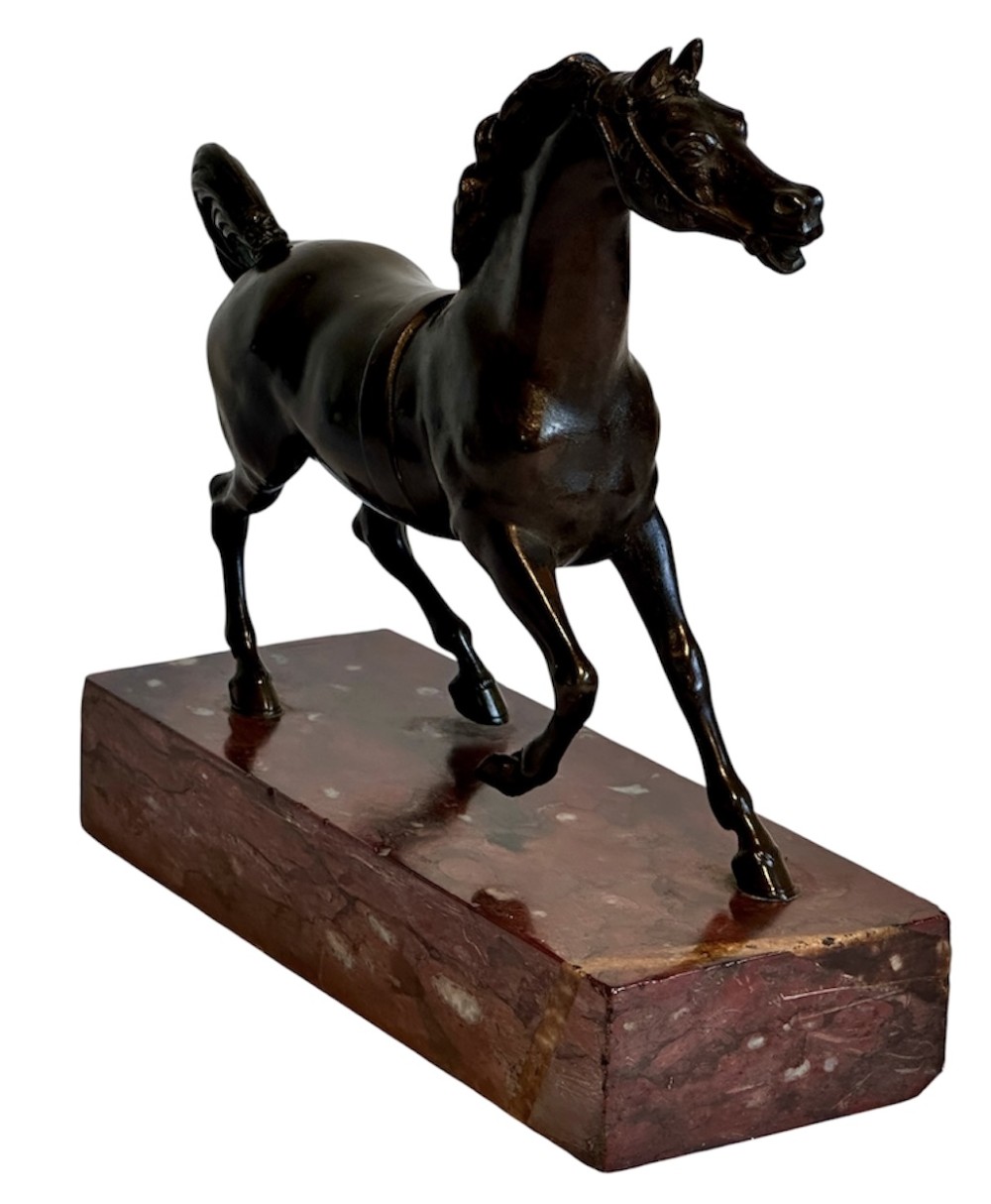 A dark patinated bronze sculpture of a trotting stallion mounted on a rectangular veined red marble plinth. View IV