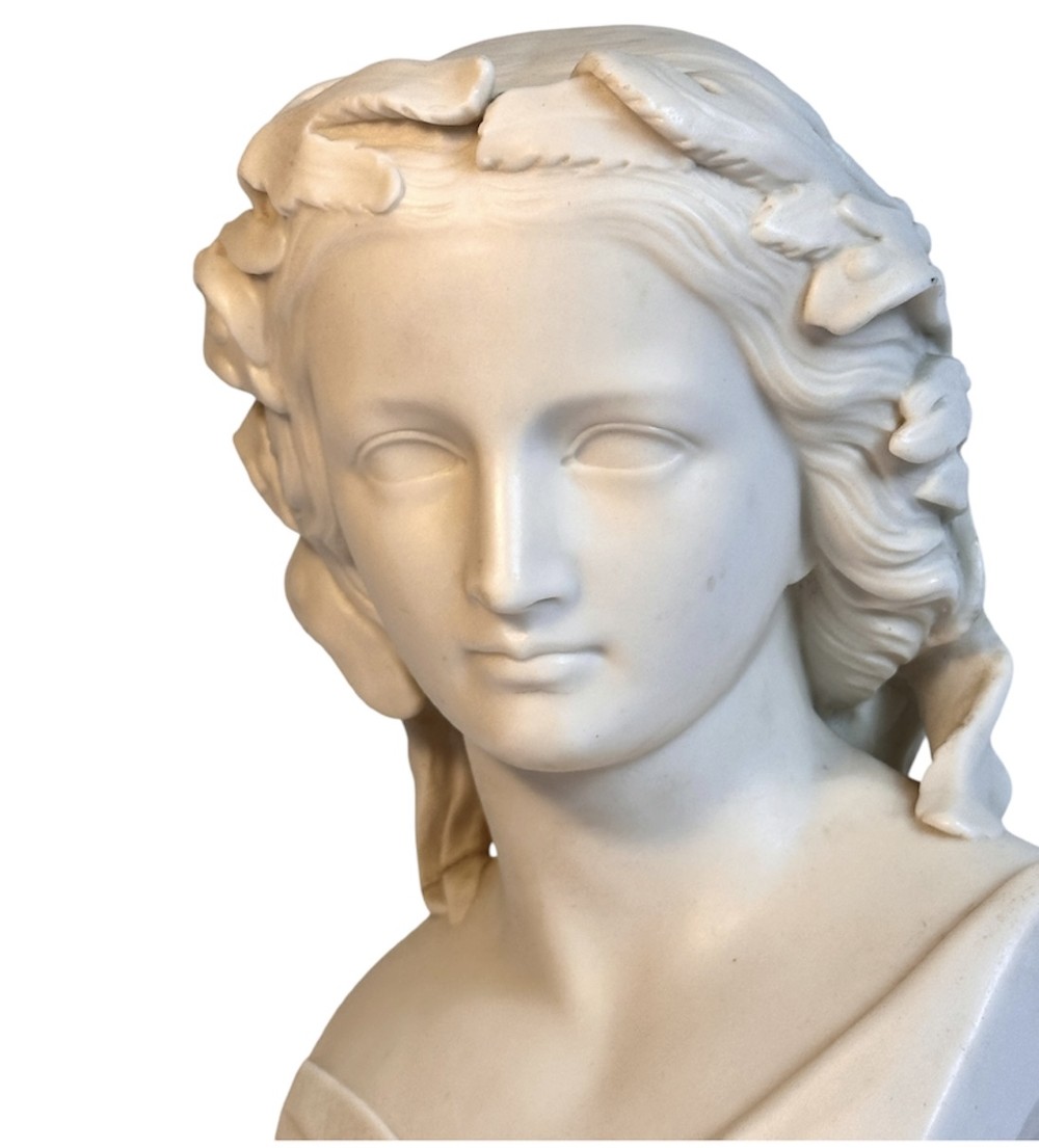 A nineteenth-century off-white Parian porcelain bust depicting a young woman with a floral headpiece draped in classical robes on a turned socle. View V