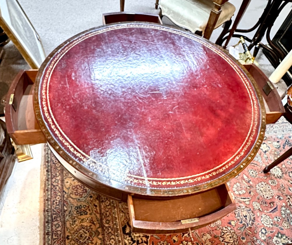 A circular antique mahogany drum table featuring a brown leather inset top, painted floral frieze drawers, and a central pedestal base on splayed legs with brass castors. View II
