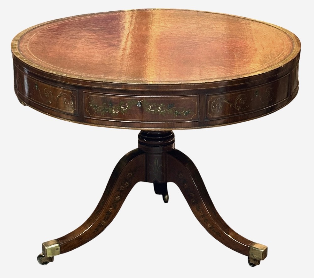 A circular antique mahogany drum table featuring a brown leather inset top, painted floral frieze drawers, and a central pedestal base on splayed legs with brass castors. View VI