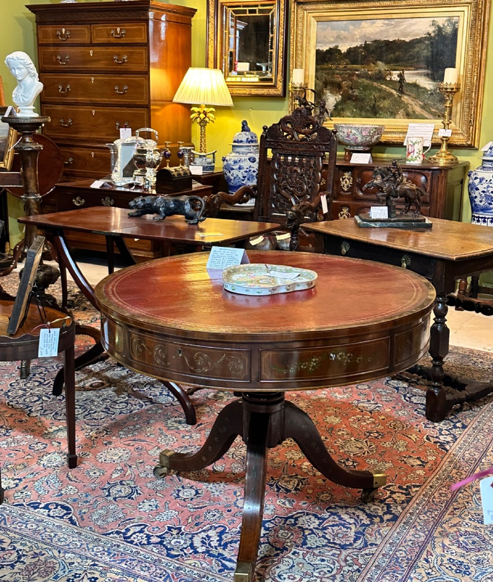 A circular antique mahogany drum table featuring a brown leather inset top, painted floral frieze drawers, and a central pedestal base on splayed legs with brass castors. View VII