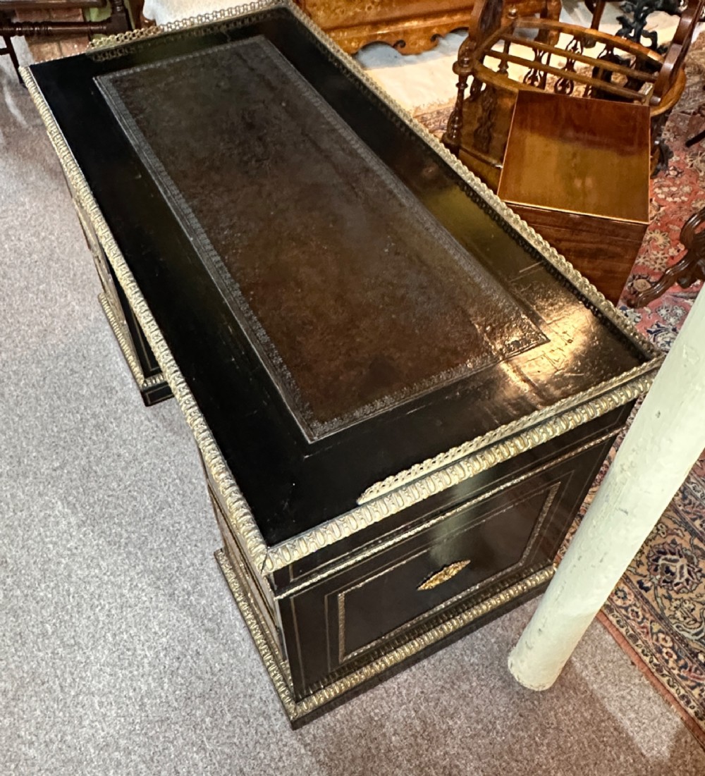 An ebonised French pedestal desk featuring red tortoiseshell and brass Boulle marquetry inlay, multiple drawers, a leather writing top, and a brass gallery. View V