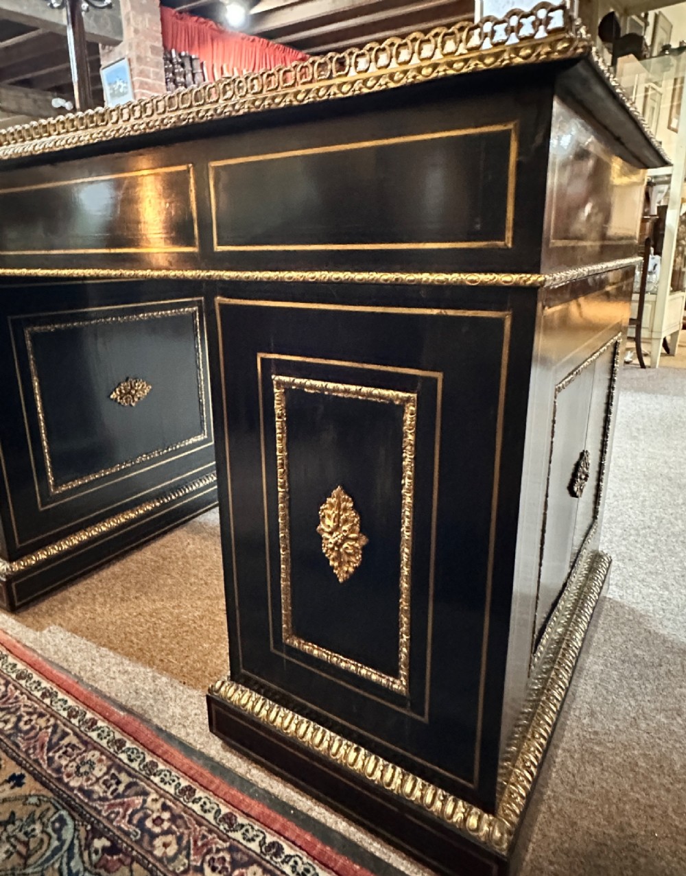 An ebonised French pedestal desk featuring red tortoiseshell and brass Boulle marquetry inlay, multiple drawers, a leather writing top, and a brass gallery. View VI