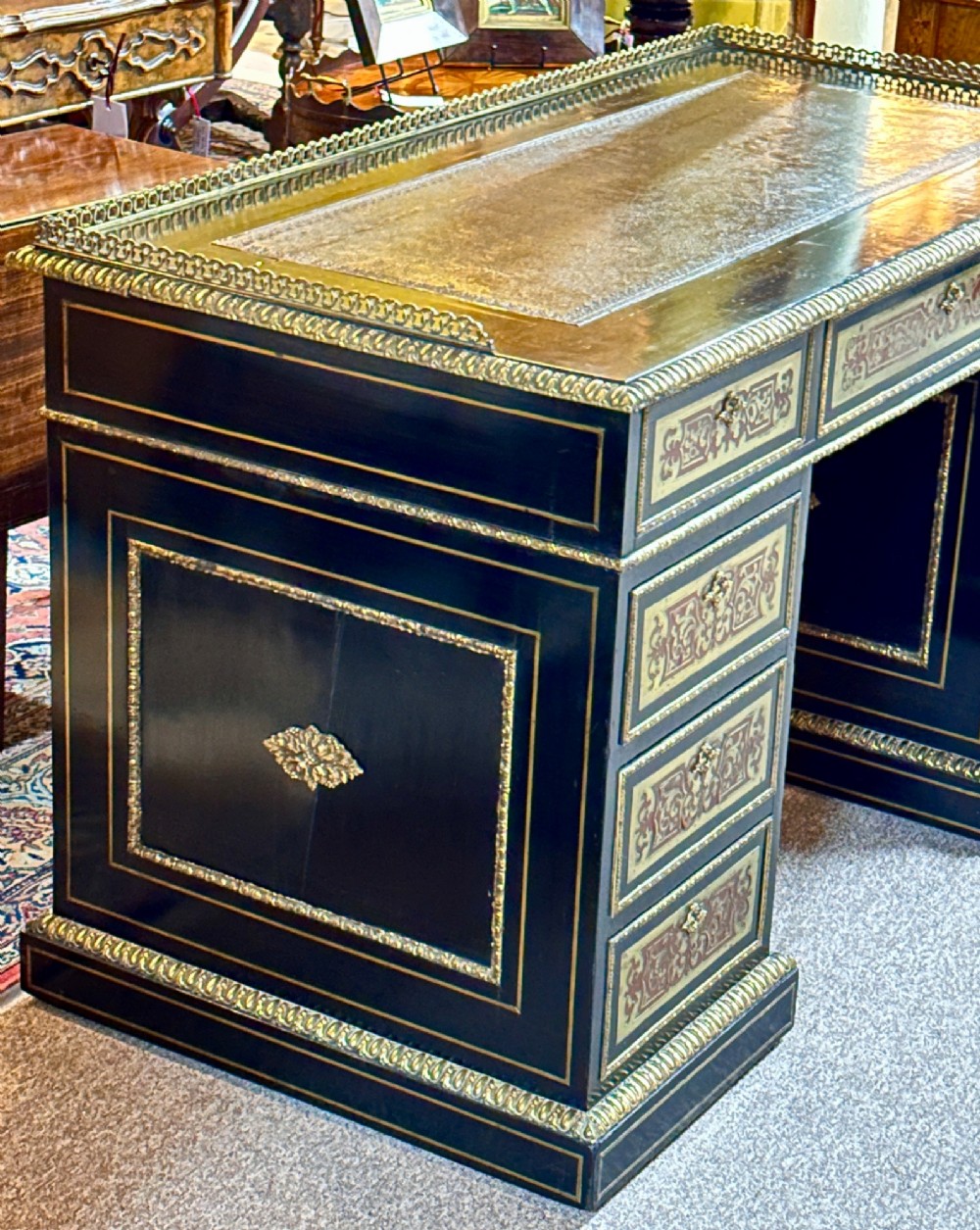 An ebonised French pedestal desk featuring red tortoiseshell and brass Boulle marquetry inlay, multiple drawers, a leather writing top, and a brass gallery. View VII