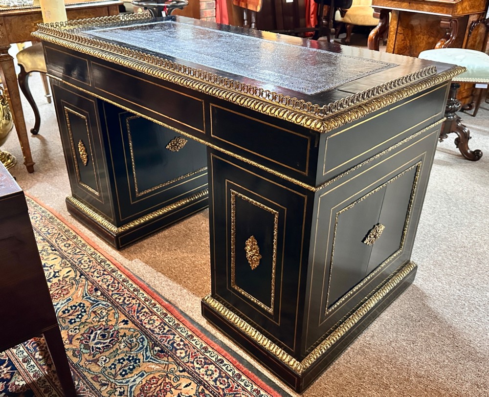 An ebonised French pedestal desk featuring red tortoiseshell and brass Boulle marquetry inlay, multiple drawers, a leather writing top, and a brass gallery. View X