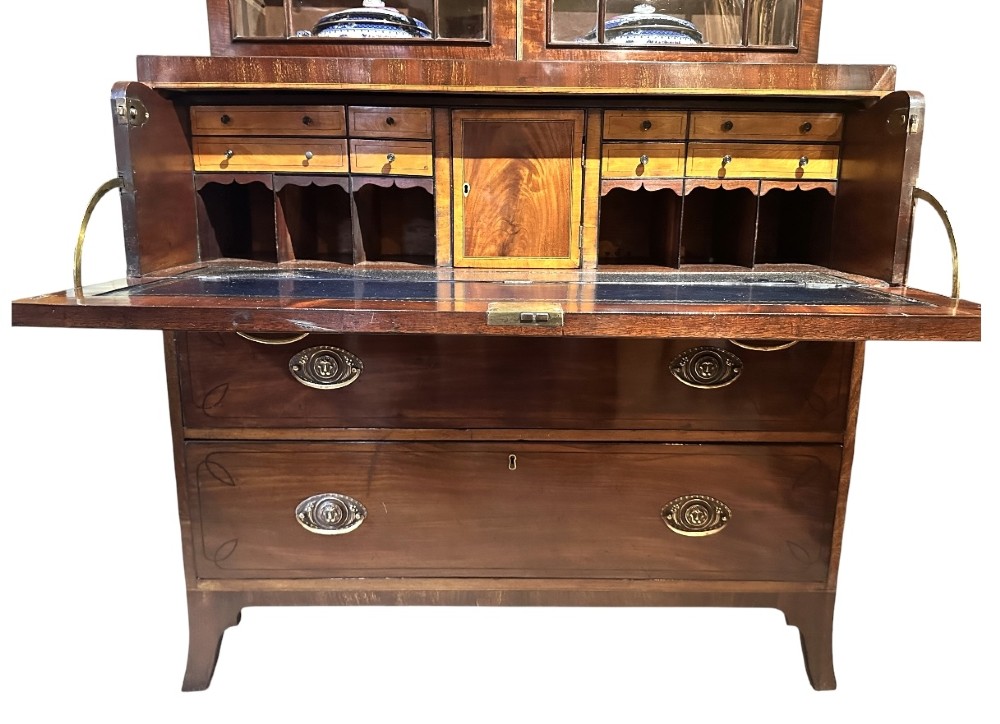 An antique Regency mahogany secretaire bookcase featuring an upper two-door glazed cabinet above a lower chest of drawers with decorative inlay and brass oval drop handles. View V