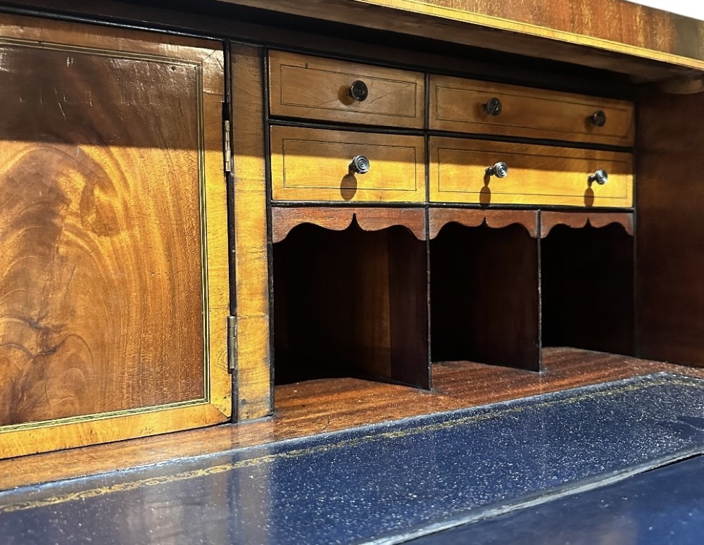 An antique Regency mahogany secretaire bookcase featuring an upper two-door glazed cabinet above a lower chest of drawers with decorative inlay and brass oval drop handles. View VI