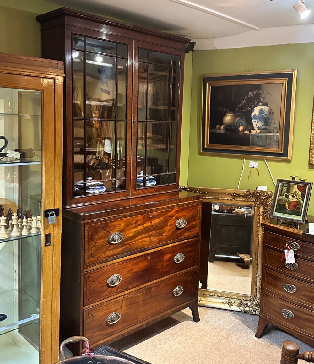 An antique Regency mahogany secretaire bookcase featuring an upper two-door glazed cabinet above a lower chest of drawers with decorative inlay and brass oval drop handles. View VIII