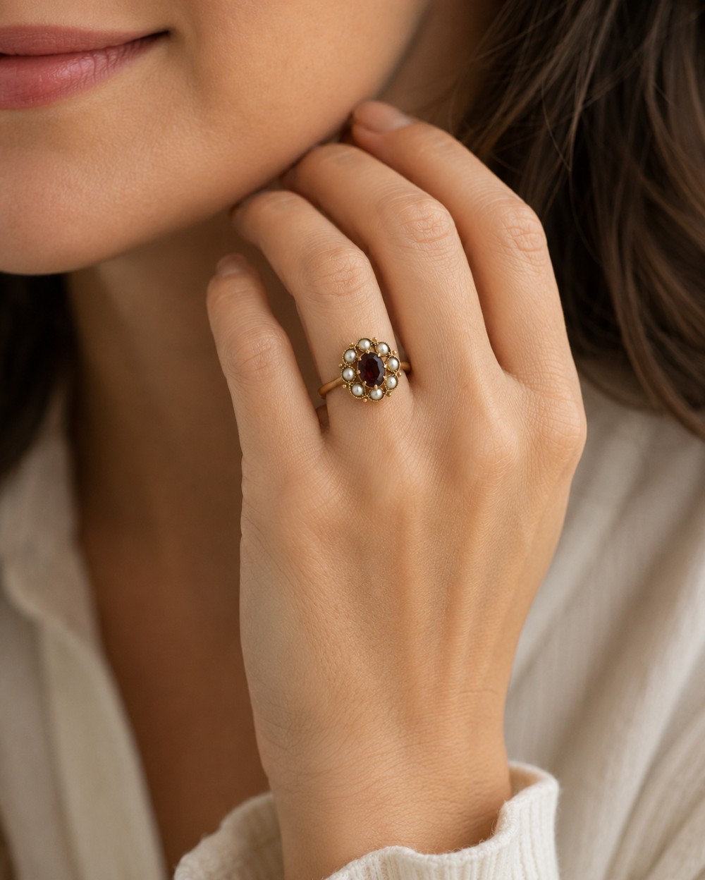 An antique yellow gold ring featuring a central oval-cut red garnet surrounded by a halo of eight seed pearls. View VII