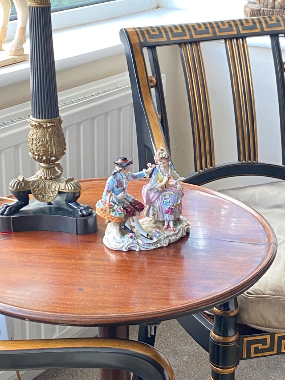 A Sitzendorf porcelain figurine group depicting an 18th-century courtly couple seated together with flower baskets on a scrollwork base with gold detailing. View II