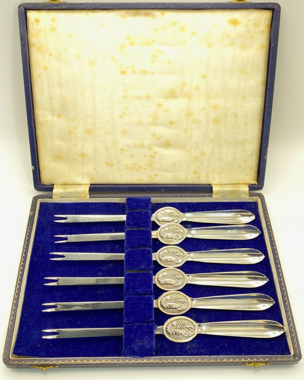 A set of six silver-plated lobster forks with slim double tines and oval medallions embossed with lobster designs on the handles. View II