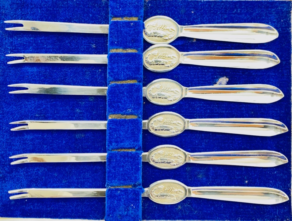 A set of six silver-plated lobster forks with slim double tines and oval medallions embossed with lobster designs on the handles. View III