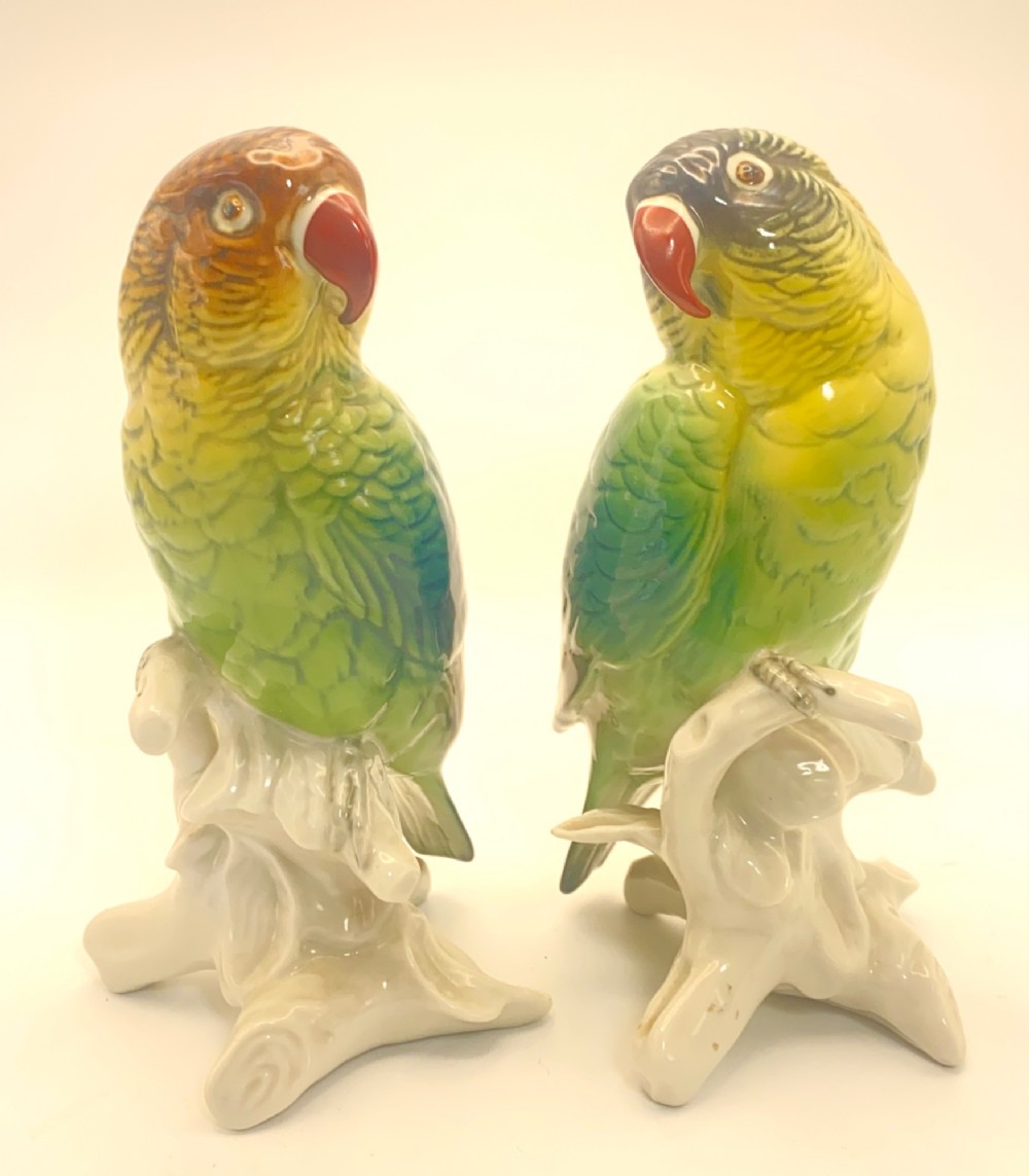 A pair of glazed porcelain parrot figurines featuring detailed green and brown feather moulding perched on off-white branch bases. View II