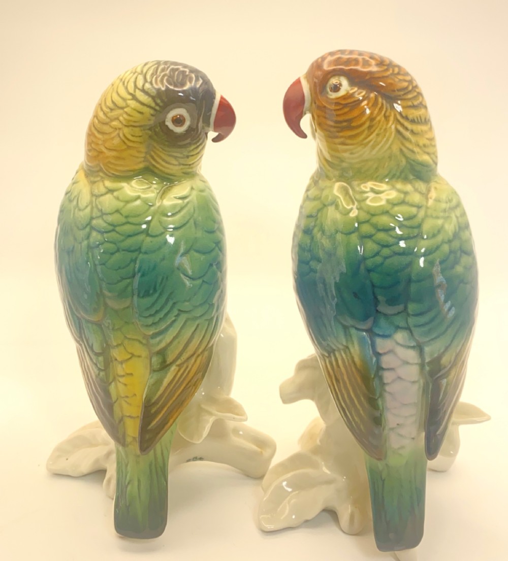 A pair of glazed porcelain parrot figurines featuring detailed green and brown feather moulding perched on off-white branch bases. View III