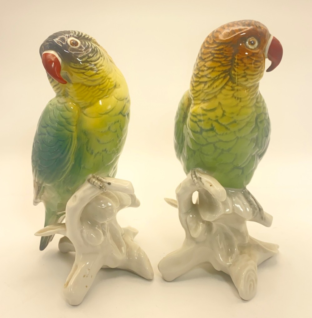 A pair of glazed porcelain parrot figurines featuring detailed green and brown feather moulding perched on off-white branch bases. View IV