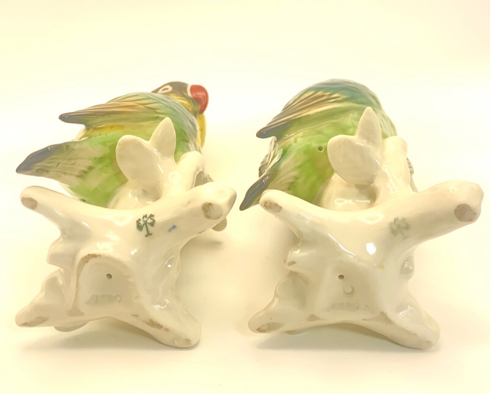 A pair of glazed porcelain parrot figurines featuring detailed green and brown feather moulding perched on off-white branch bases. View V