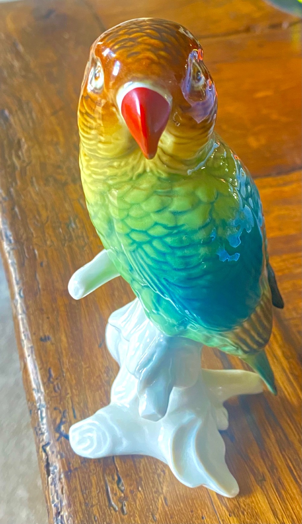 A pair of glazed porcelain parrot figurines featuring detailed green and brown feather moulding perched on off-white branch bases. View VIII
