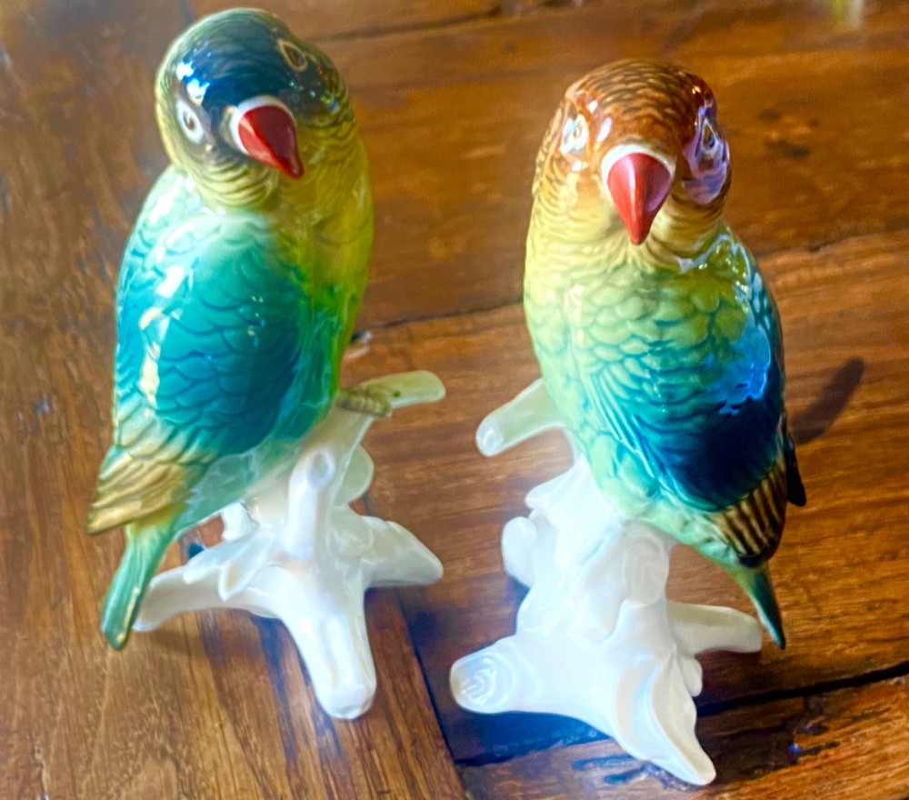 A pair of glazed porcelain parrot figurines featuring detailed green and brown feather moulding perched on off-white branch bases. View IX