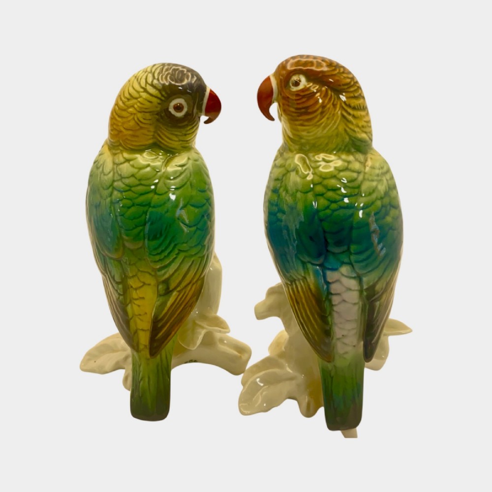 A pair of glazed porcelain parrot figurines featuring detailed green and brown feather moulding perched on off-white branch bases. View VI