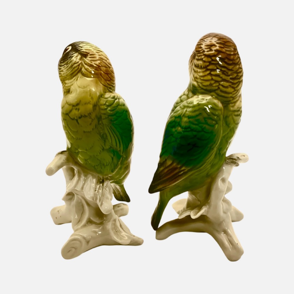 A pair of glazed porcelain parrot figurines featuring detailed green and brown feather moulding perched on off-white branch bases. View VII