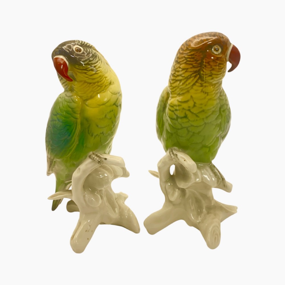 A pair of glazed porcelain parrot figurines featuring detailed green and brown feather moulding perched on off-white branch bases. View VIII