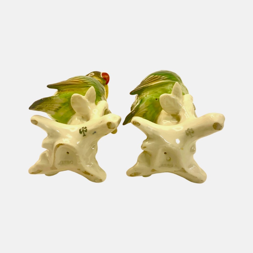 A pair of glazed porcelain parrot figurines featuring detailed green and brown feather moulding perched on off-white branch bases. View IX