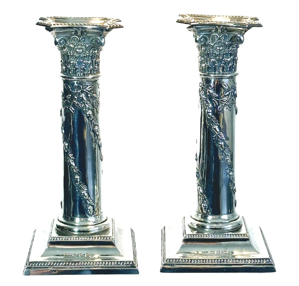A pair of polished silver column candlesticks featuring Corinthian capitals, foliate swags, and stepped beaded bases.