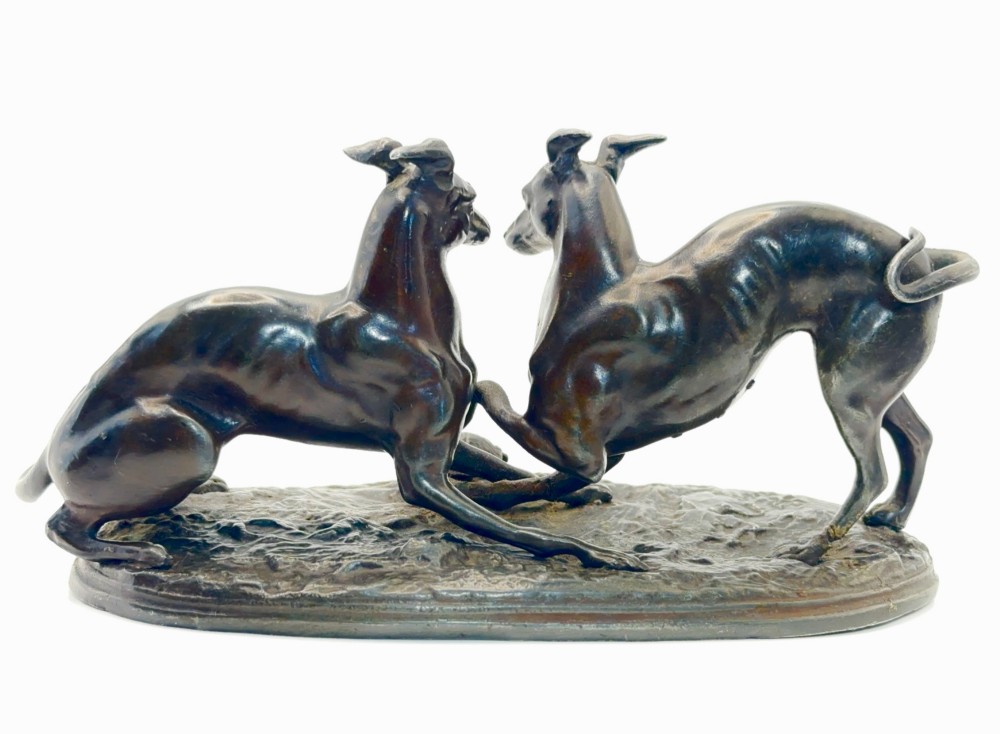 An antique dark brown spelter sculpture depicting two playing greyhounds positioned over a small tortoise on an oval base.