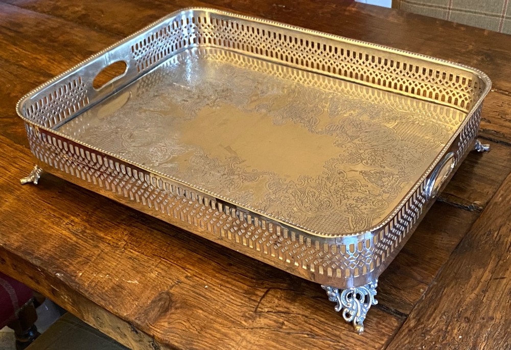 A rectangular silver-plated gallery tray featuring pierced fretwork sides, integrated oval hand-holds, an engraved surface, and ornate scrolled feet. View V