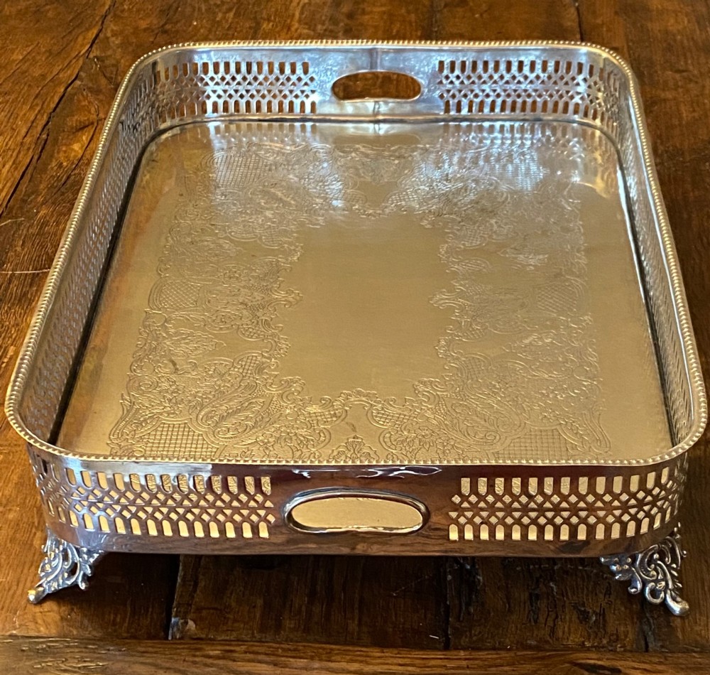 A rectangular silver-plated gallery tray featuring pierced fretwork sides, integrated oval hand-holds, an engraved surface, and ornate scrolled feet.