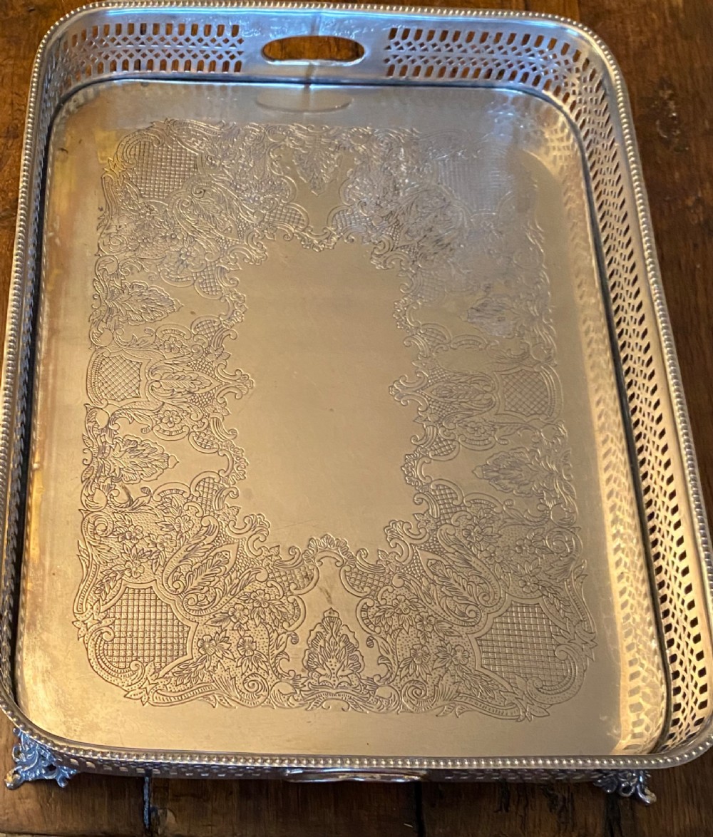 A rectangular silver-plated gallery tray featuring pierced fretwork sides, integrated oval hand-holds, an engraved surface, and ornate scrolled feet. View VI