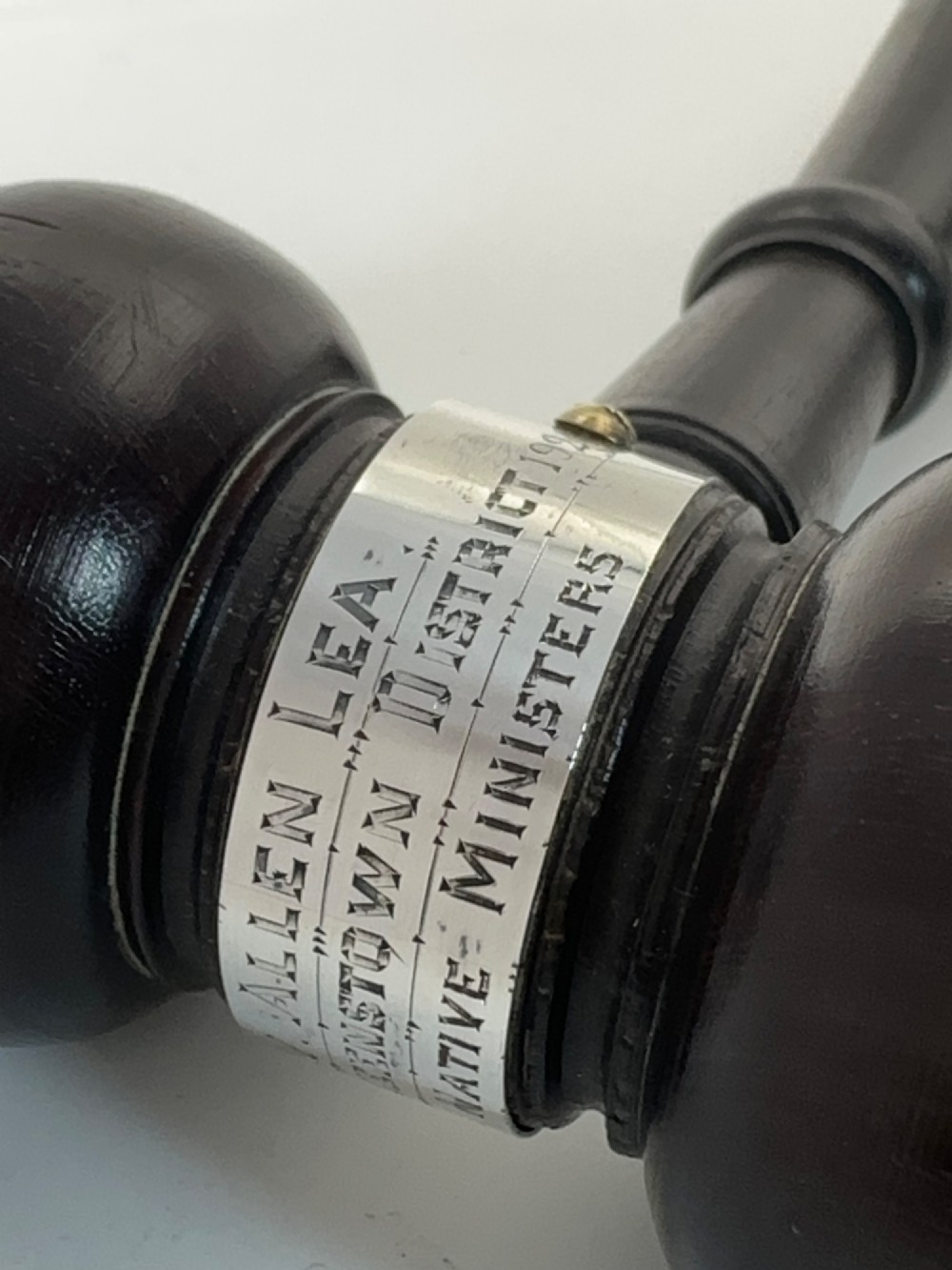 A turned dark wood ceremonial gavel featuring a central silver presentation band secured with small screws. View V