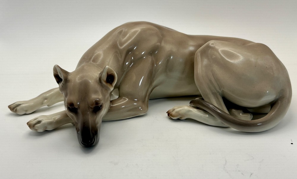 A glazed Nymphenburg porcelain figurine depicting a recumbent Great Dane dog in taupe grey and neutral tones.