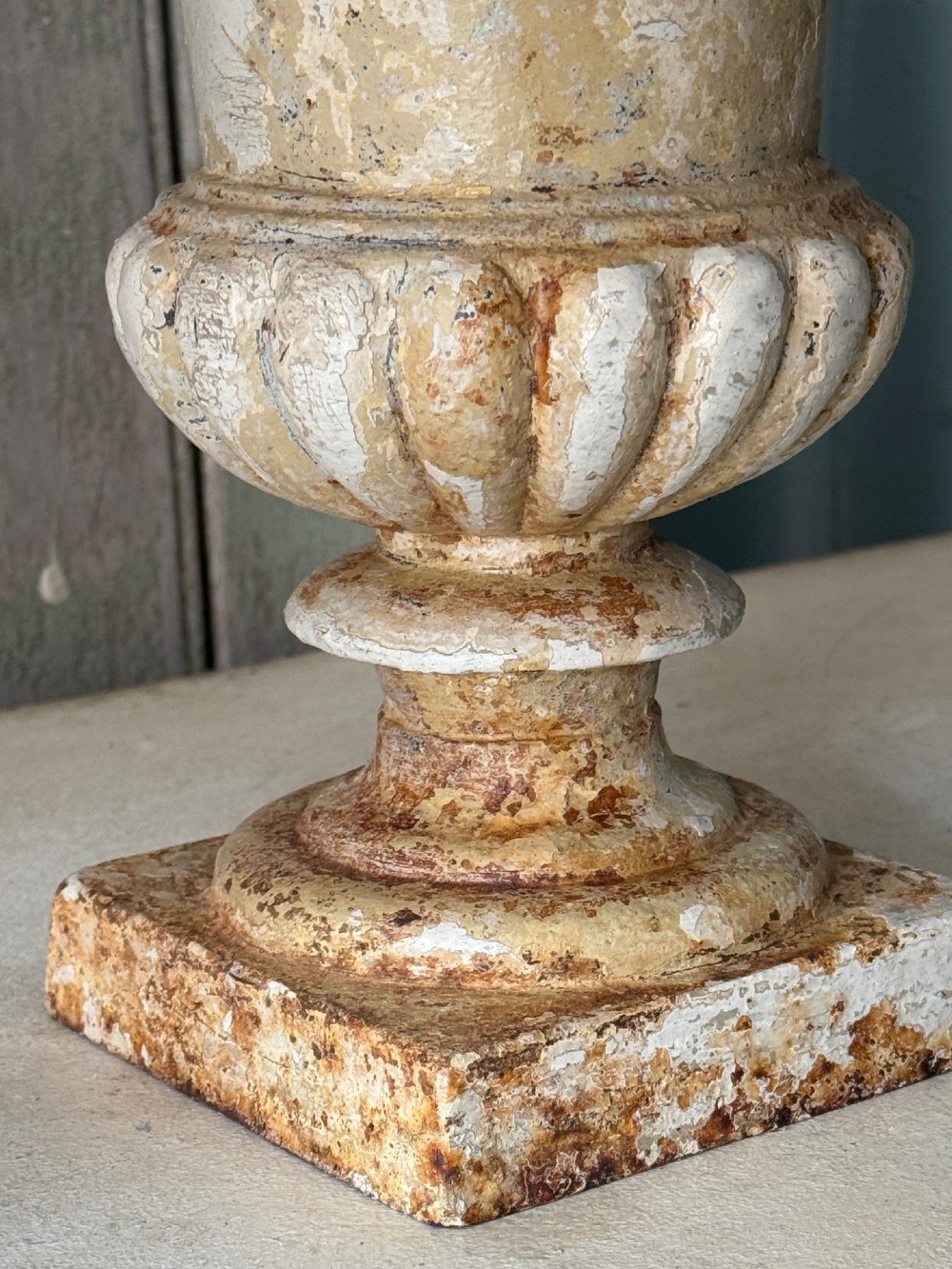 A pair of antique French cast iron garden urns with fluted bodies, square bases, and weathered off-white painted finishes showing natural rust patina. View III