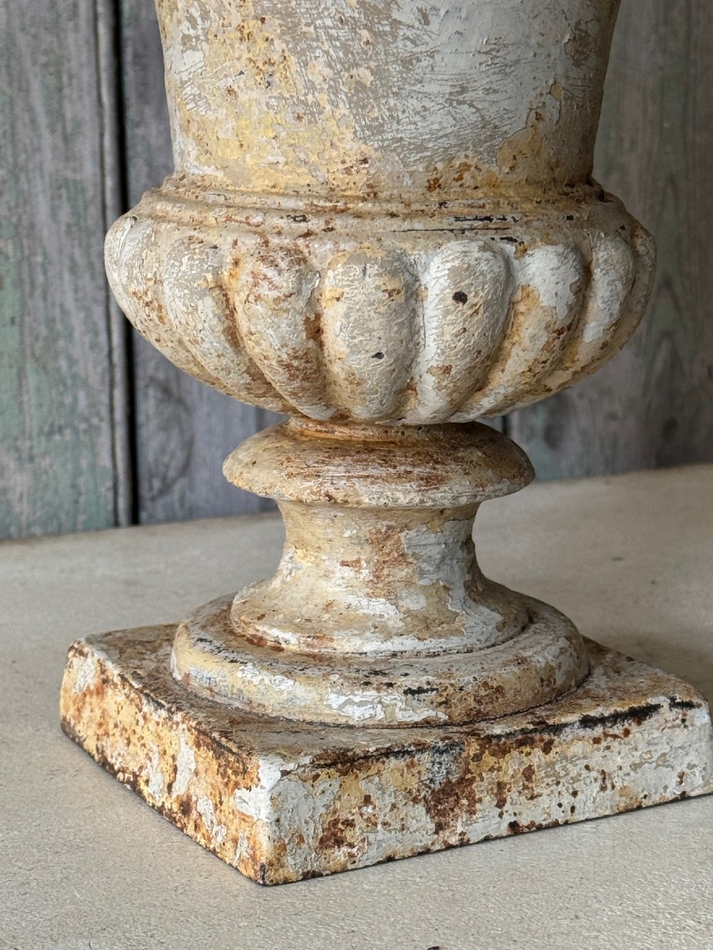 A pair of antique French cast iron garden urns with fluted bodies, square bases, and weathered off-white painted finishes showing natural rust patina. View IV