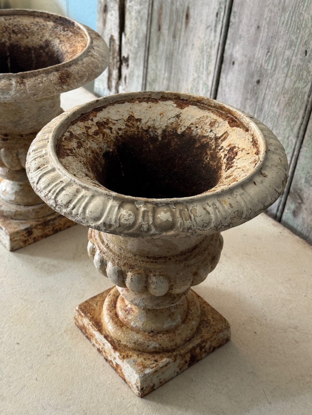 A pair of antique French cast iron garden urns with fluted bodies, square bases, and weathered off-white painted finishes showing natural rust patina. View VI