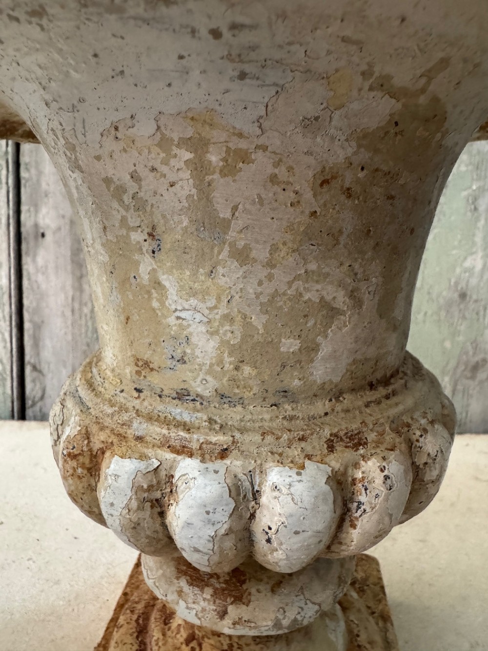A pair of antique French cast iron garden urns with fluted bodies, square bases, and weathered off-white painted finishes showing natural rust patina. View VII