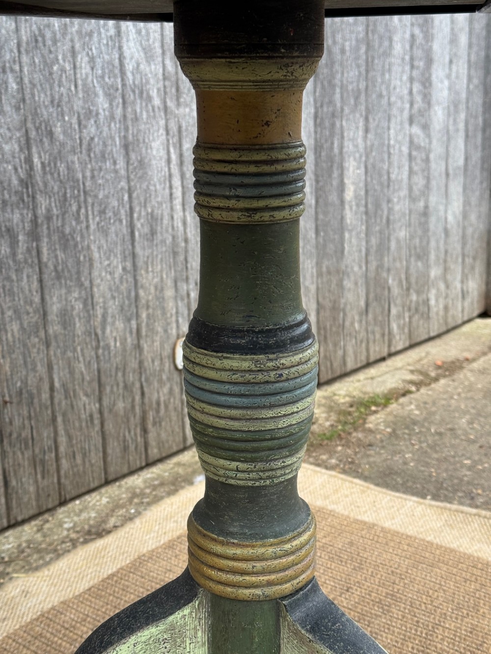 A Victorian circular tilt-top side table featuring hand-painted geometric patterns in sage green, olive, and cream resting on a turned stem with tripod legs. View VI
