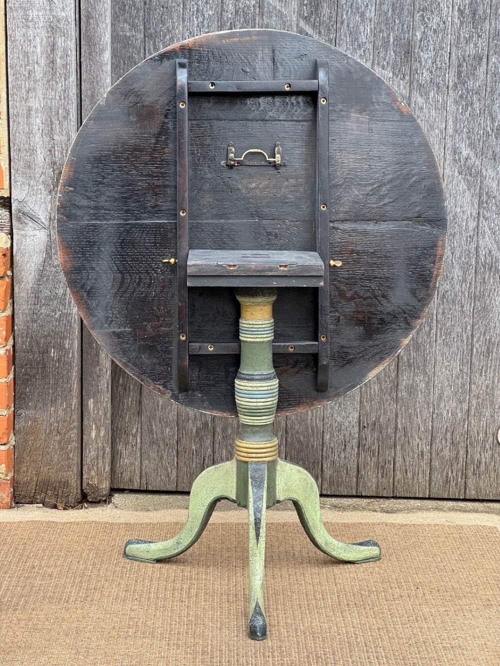 A Victorian circular tilt-top side table featuring hand-painted geometric patterns in sage green, olive, and cream resting on a turned stem with tripod legs. View VIII