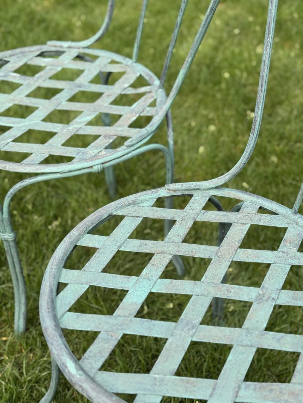 A weathered green painted wrought iron bistro set featuring a round pedestal table and two hoop-back chairs with lattice seats. View VII