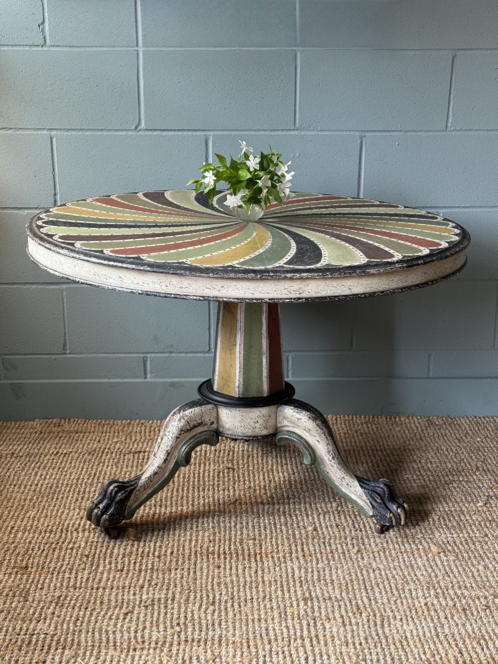 A Victorian circular tilt-top table featuring a hand-painted swirling polychrome petal pattern across its surface, resting on a distressed carved tripod base. View II