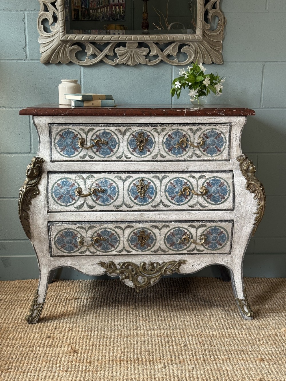 A nineteenth-century French bombee chest of drawers featuring a later hand-painted pattern, a dark marble top, and ornate gilt bronze mounts. View II